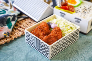 Mini Pork Cutlets in a house-shaped bento with shredded cabbage, rice, tomatoes, and half an egg.