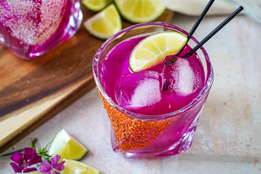 Close up of Prickly Pear Margarita in a glass with ice cubes and a lime wedge.