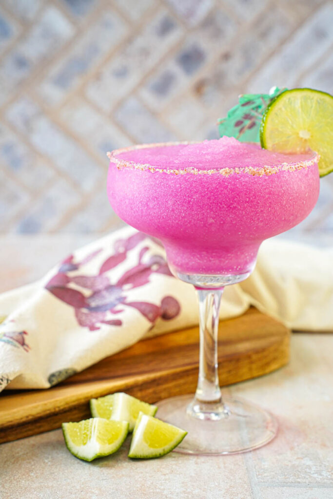 Side view of a Frozen Prickly Pear Margarita with a salt rim and a lime slice and green umbrella garnish.