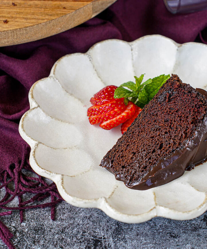 A slice of Red Wine Chocolate Cake on a plate with a sliced strawberry and mint sprig.