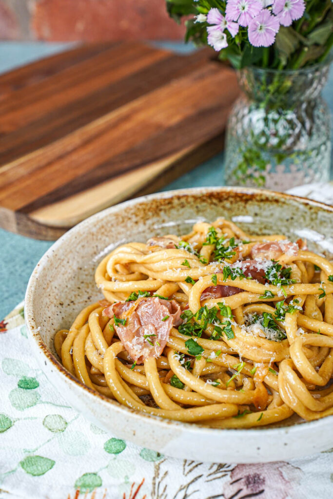 Bucatini in a bowl with caramelized onions and prosciutto.