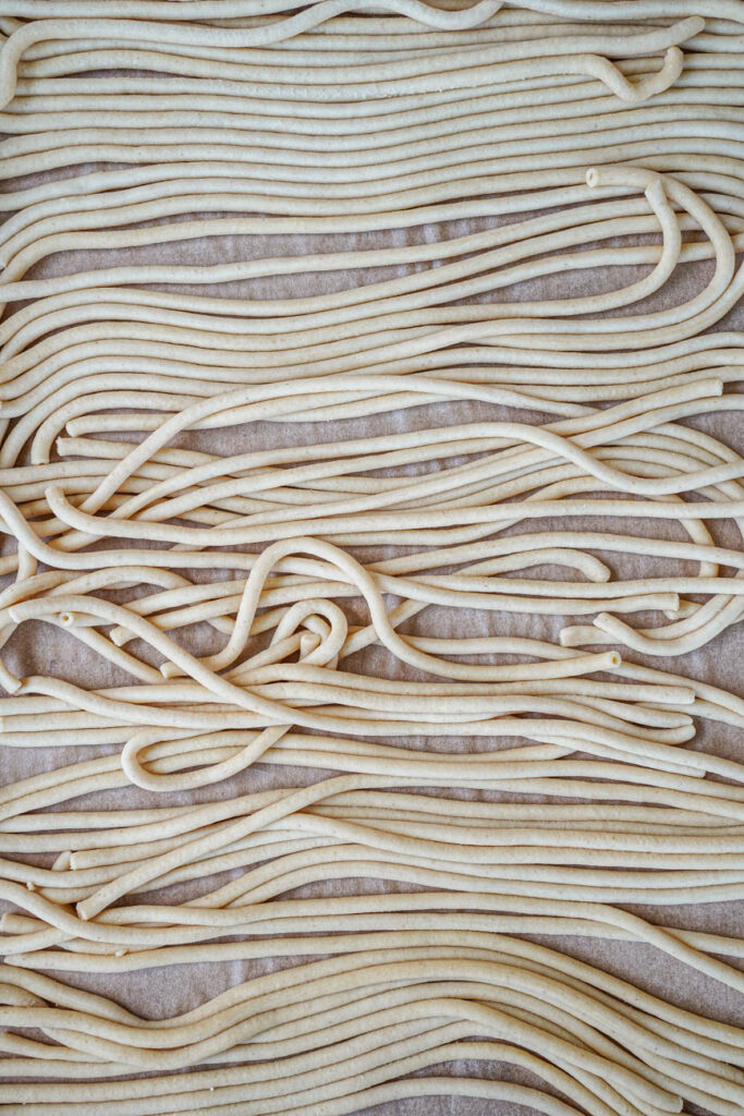 Bucatini arranged on a parchment-lined baking sheet.