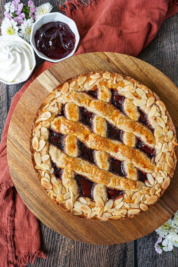 Aerial view of Linzer Torte on a wooden board next to red currant jelly and whipped cream.