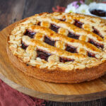 Linzer Torte on a wooden board with jam and whipped cream in the background.