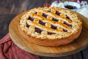 Linzer Torte on a wooden board with jam and whipped cream in the background.