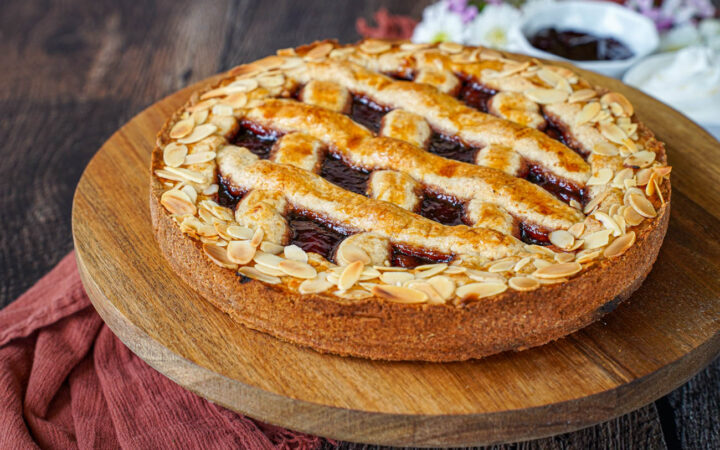 Linzer Torte on a wooden board with jam and whipped cream in the background.