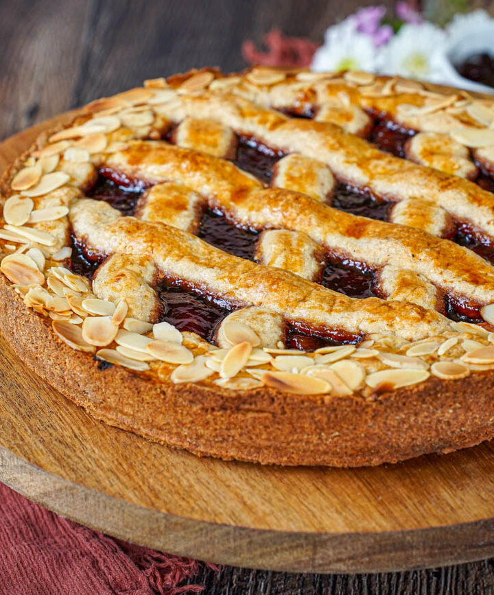 Linzer Torte on a wooden board with jam and whipped cream in the background.