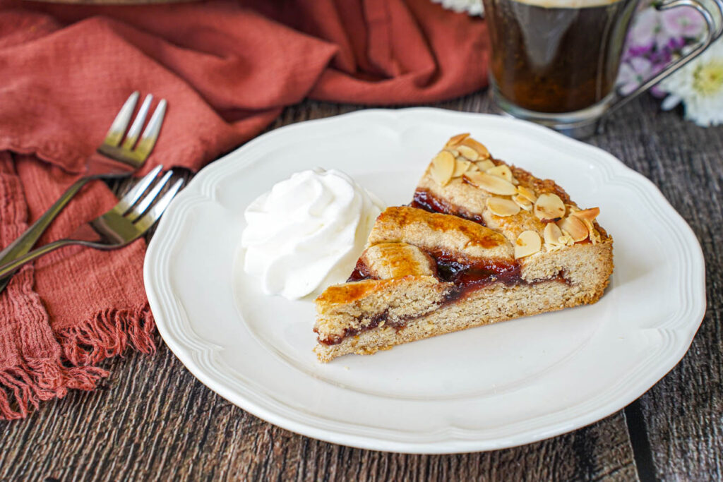 A slice of Linzer Torte on a plate with a dollop of whipped cream.