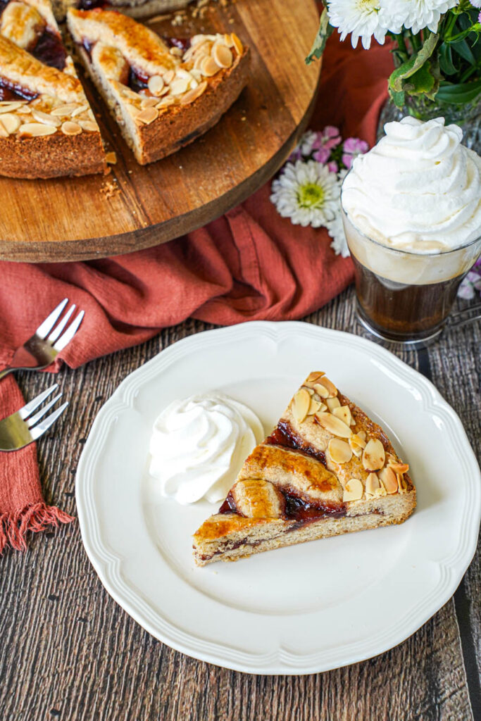 A slice of Linzer Torte on a plate next to more on a wooden board and Einspänner in a glass.