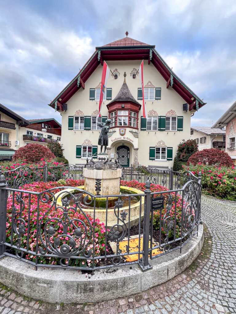 Town hall in St. Gilgen with a fountain and fence in the front.