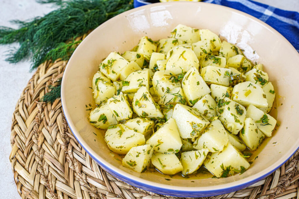 Patatosalata (Herby Potato Salad) in a blue and tan bowl next to a bunch of dill.
