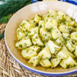 Patatosalata (Herby Potato Salad) in a blue and tan bowl next to a bunch of dill.