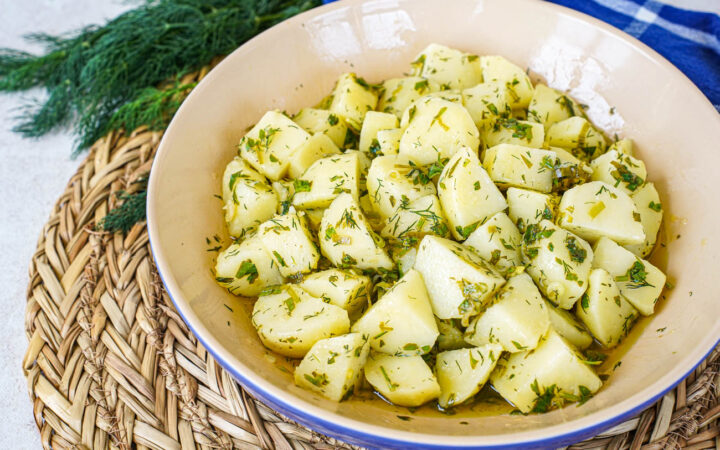Patatosalata (Herby Potato Salad) in a blue and tan bowl next to a bunch of dill.
