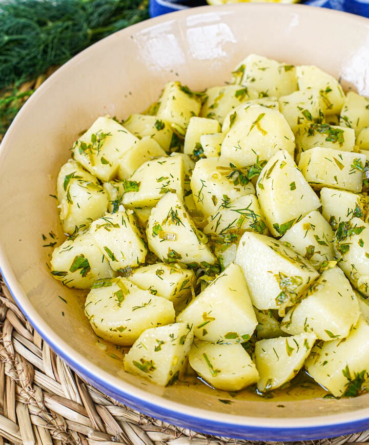 Patatosalata (Herby Potato Salad) in a blue and tan bowl next to a bunch of dill.
