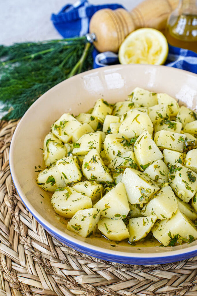 Close up of Patatosalata (Herby Potato Salad) in a bowl with dill and lemon in the background.