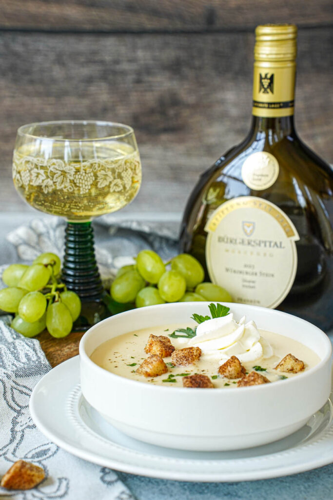 Side view of Fränkische Weinsuppe (Franconian Wine Soup) in a white bowl with a bottle of wine and a glass of wine in the background.