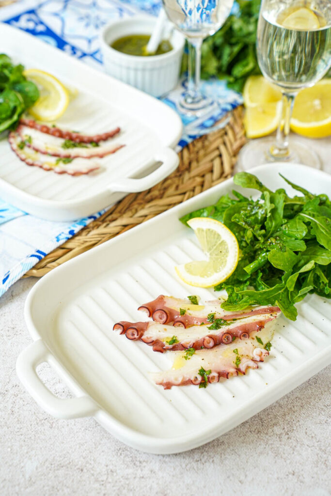 Close up of Grilled Octopus Carpaccio on two plates with two wine glasses in the background.