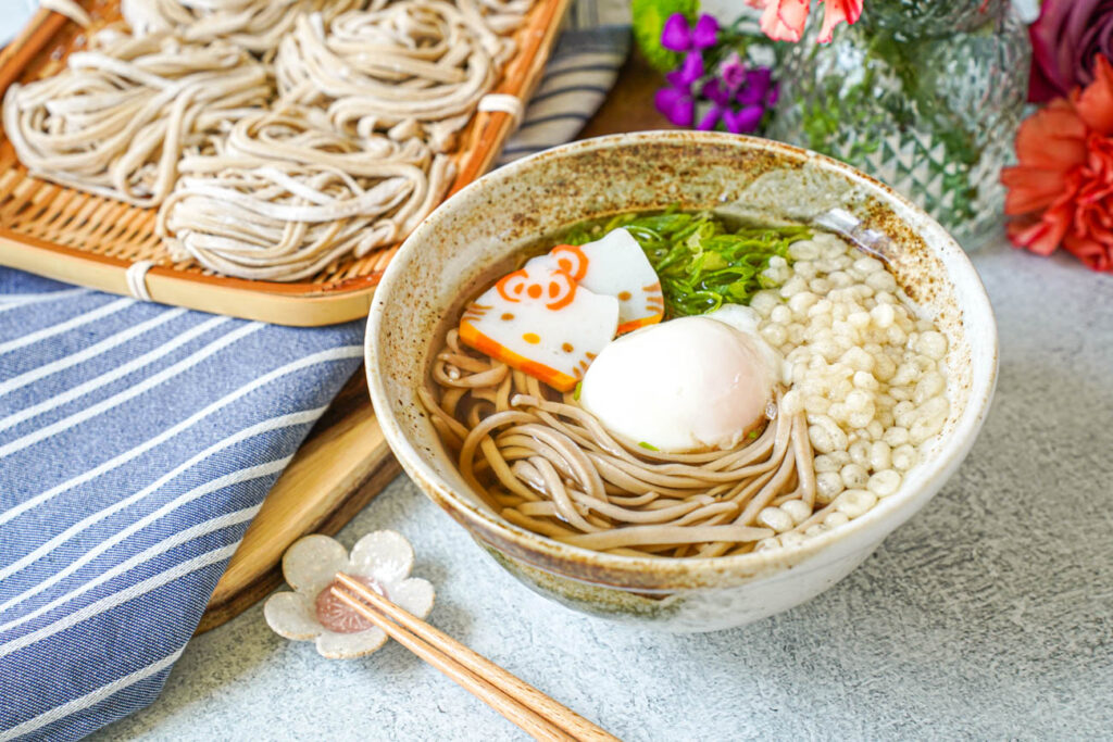 Homemade Soba in a bowl with broth, fish cakes, green onion, and tenkasu.