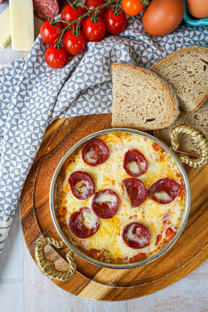 Aerial view of Menemen (Tomato and Pepper Scrambled Eggs) in a copper bowl next to bread slices and cherry tomatoes.