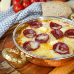 Menemen (Tomato and Pepper Scrambled Eggs) in a copper pan with melted cheese and sausage slices.