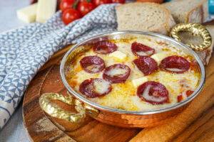 Menemen (Tomato and Pepper Scrambled Eggs) in a copper pan with melted cheese and sausage slices.