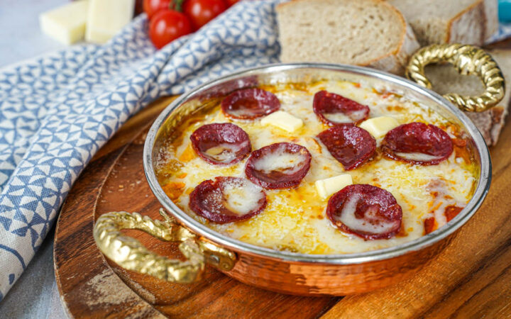 Menemen (Tomato and Pepper Scrambled Eggs) in a copper pan with melted cheese and sausage slices.