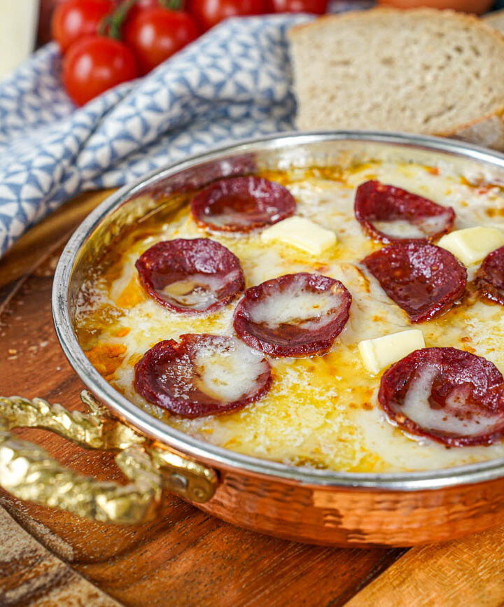 Menemen (Tomato and Pepper Scrambled Eggs) in a copper pan with melted cheese and sausage slices.