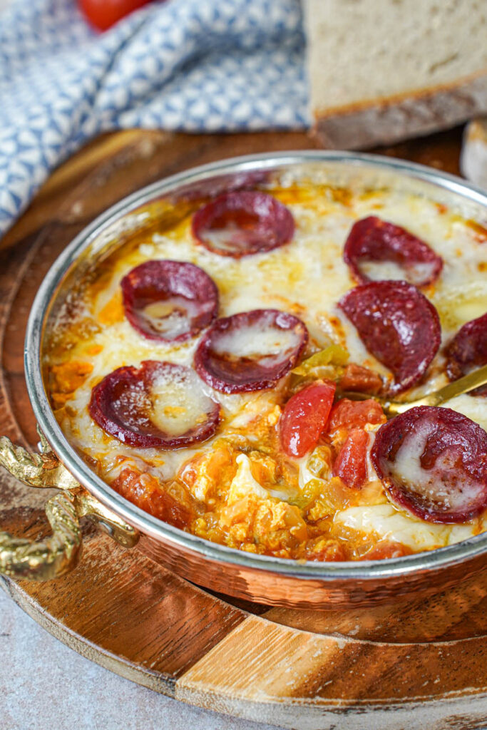 A spoon scooping up Menemen (Tomato and Pepper Scrambled Eggs) in a copper bowl.