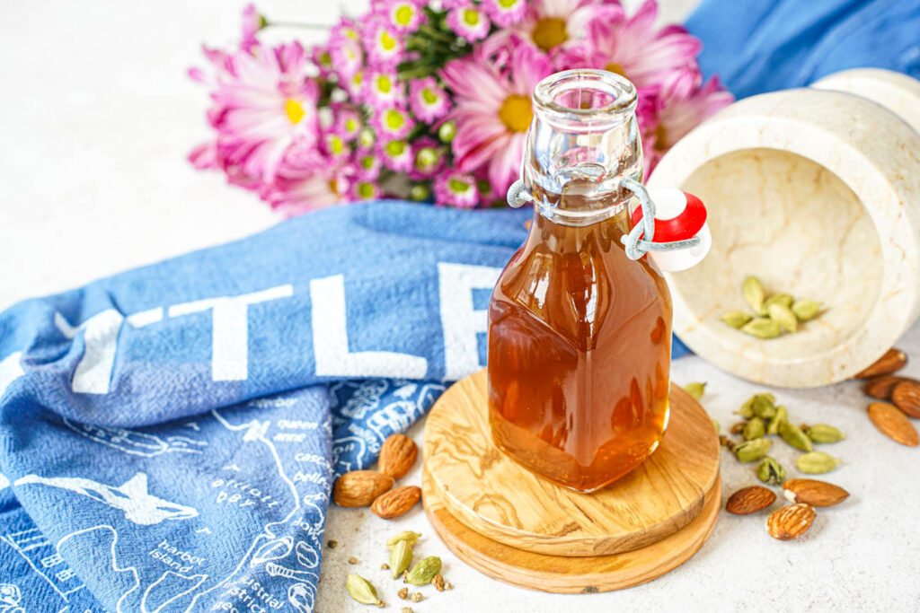 Almond Cardamom Syrup in a jar on two wooden coasters next to almonds and cardamom pods.