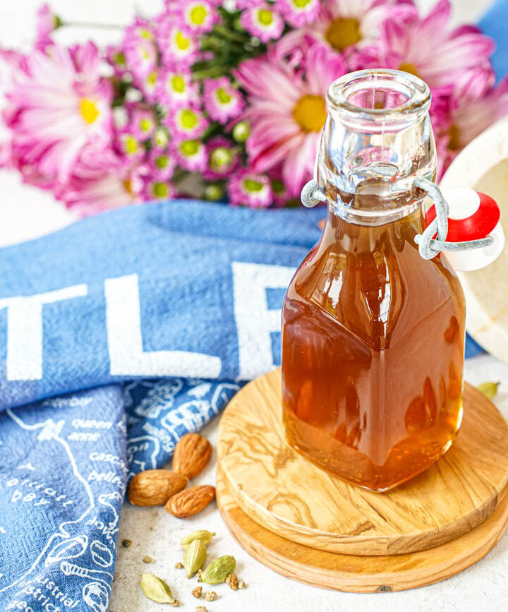 Almond Cardamom Syrup in a glass jar next to a mortar, cardamom pods, and almonds.