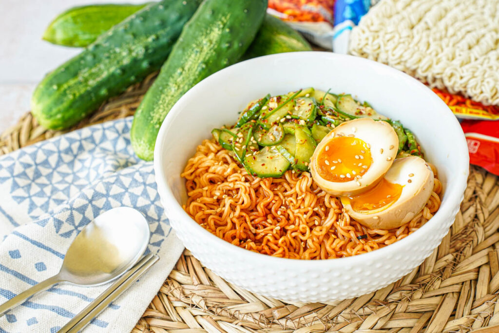 Korean Cucumber Salad Ramyeon in a white bowl with cucumber salad with a halved egg.