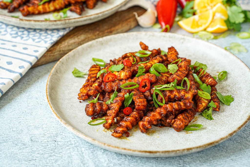 Masala Fries on a plate with sliced red chilies, scallions, and cilantro.