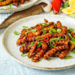 Masala Fries on a plate with sliced scallions, red Chile, and cilantro.