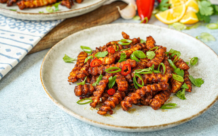 Masala Fries on a plate with sliced scallions, red Chile, and cilantro.