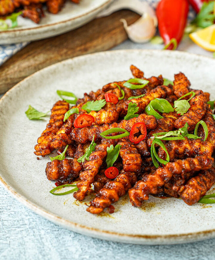 Masala Fries on a plate with sliced scallions, red Chile, and cilantro.