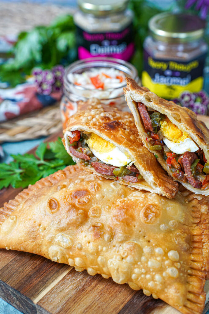Pate Kòde (Haitian Fried Patties) on a wooden board with one cut in half to show hot dog and hard boiled egg filling.