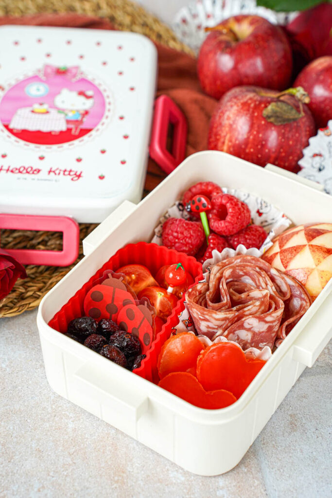 Close up of Red Bento Box with apples and roses in the background.