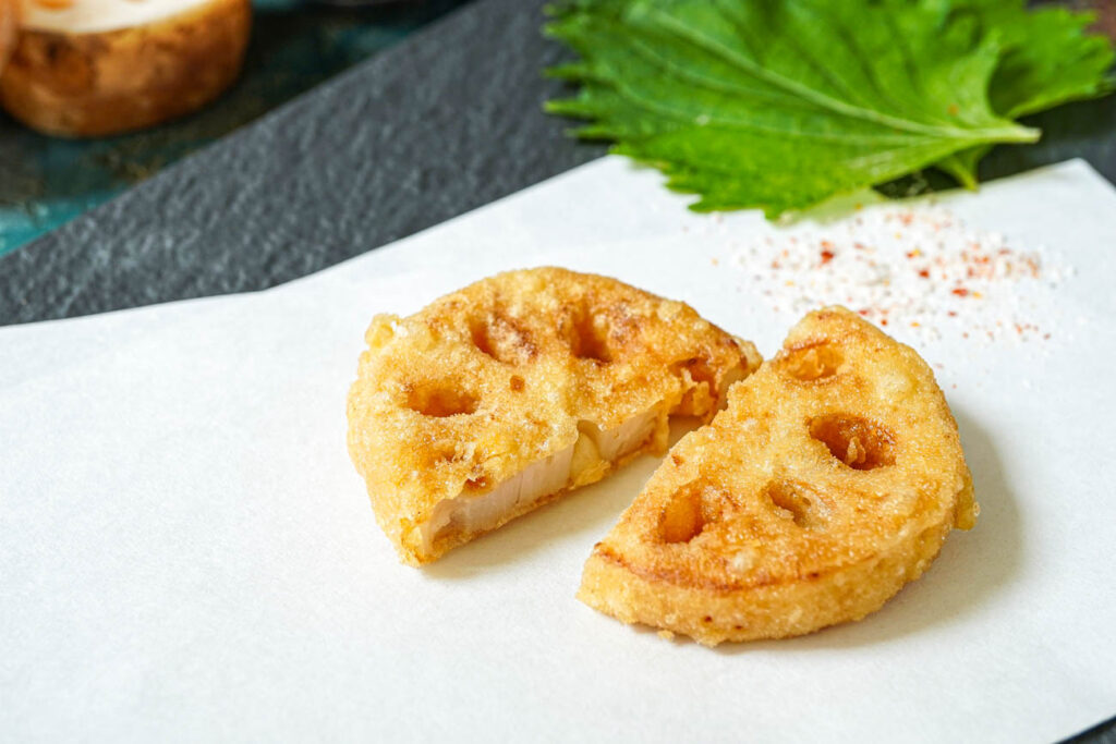 Two Lotus Root Tempura slices on a folded white sheet of paper.