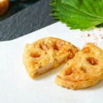 Two slices of lotus root tempura on a folded white sheet of paper.