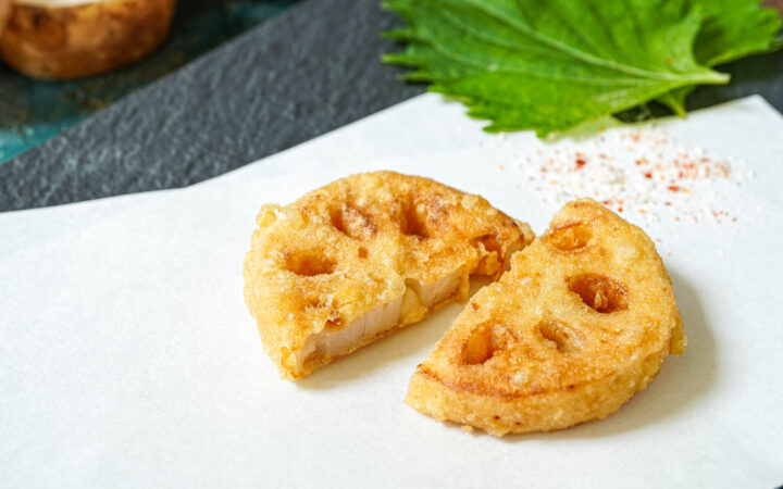 Two slices of lotus root tempura on a folded white sheet of paper.