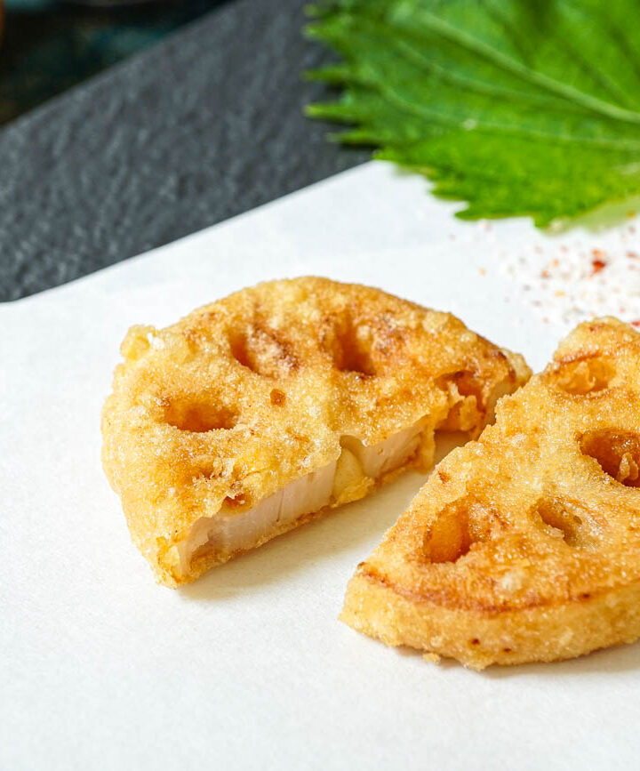 Two slices of lotus root tempura on a folded white sheet of paper.