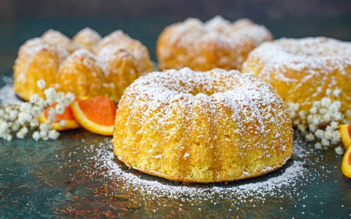 Four small Meskouta (Moroccan Orange Cakes) covered in powdered sugar.