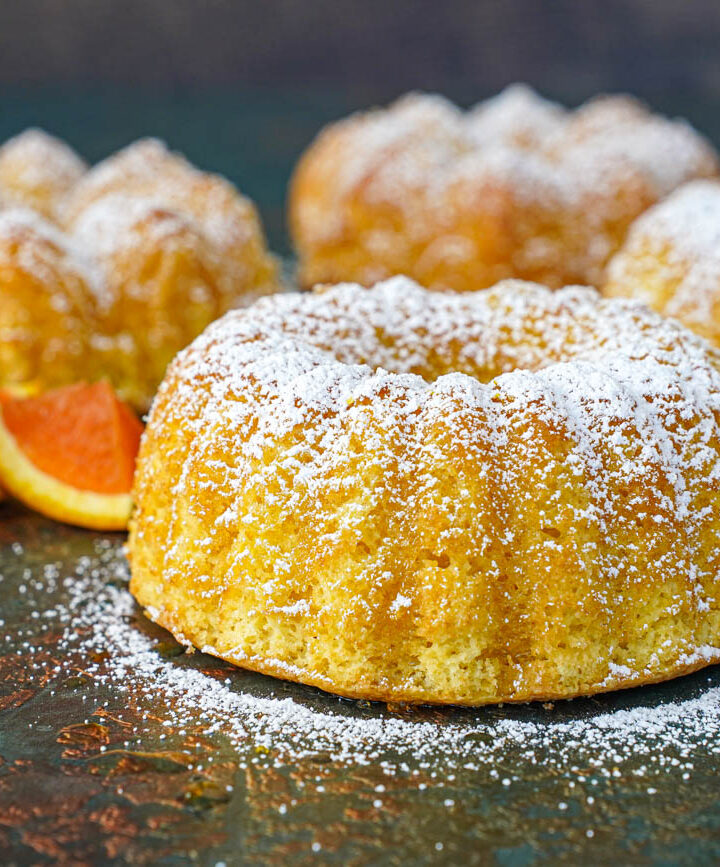 Four small Meskouta (Moroccan Orange Cakes) covered in powdered sugar.