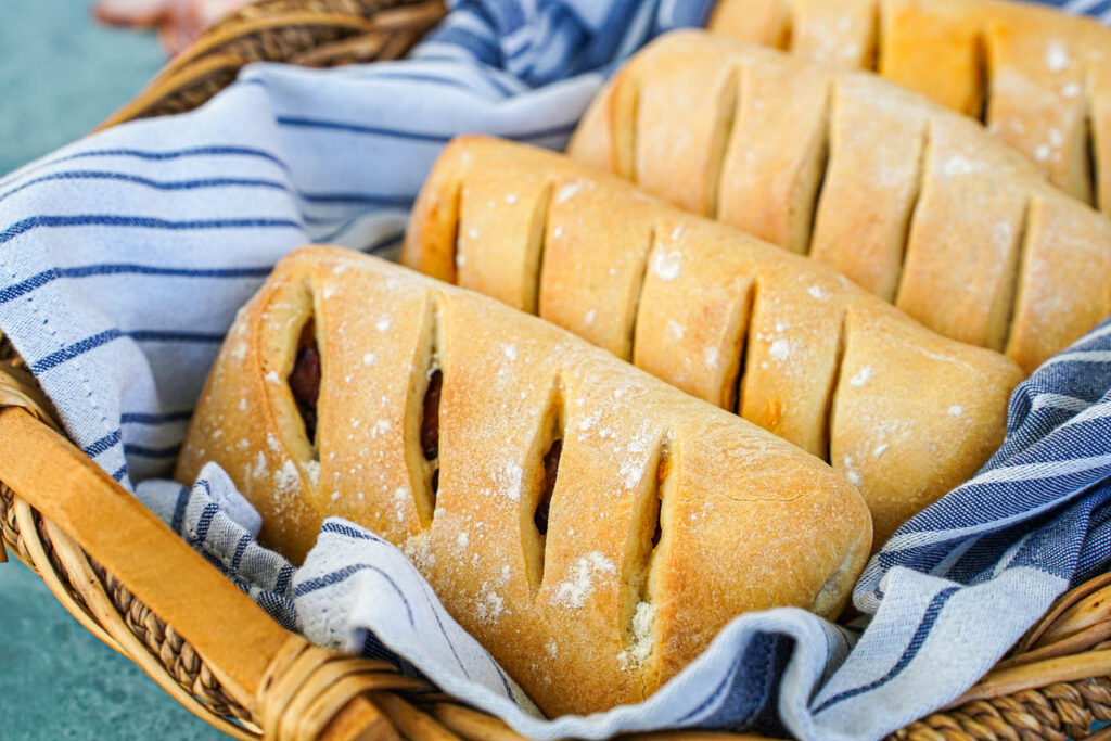 Close up of Pão com Chouriço (Portuguese Chouriço Bread) in a basket with a white and grey striped towel.