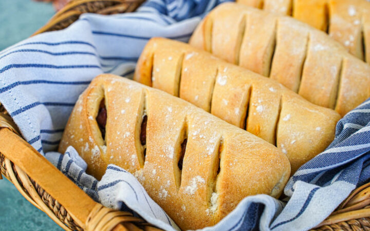 Pão com Chouriço (Portuguese Chouriço Bread) in a basket with a grey and white striped towel.