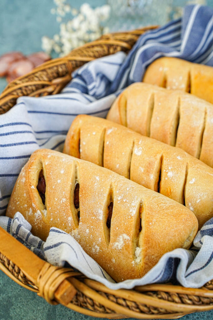 Pão com Chouriço (Portuguese Chouriço Bread) in a basket with a white and grey striped towel.