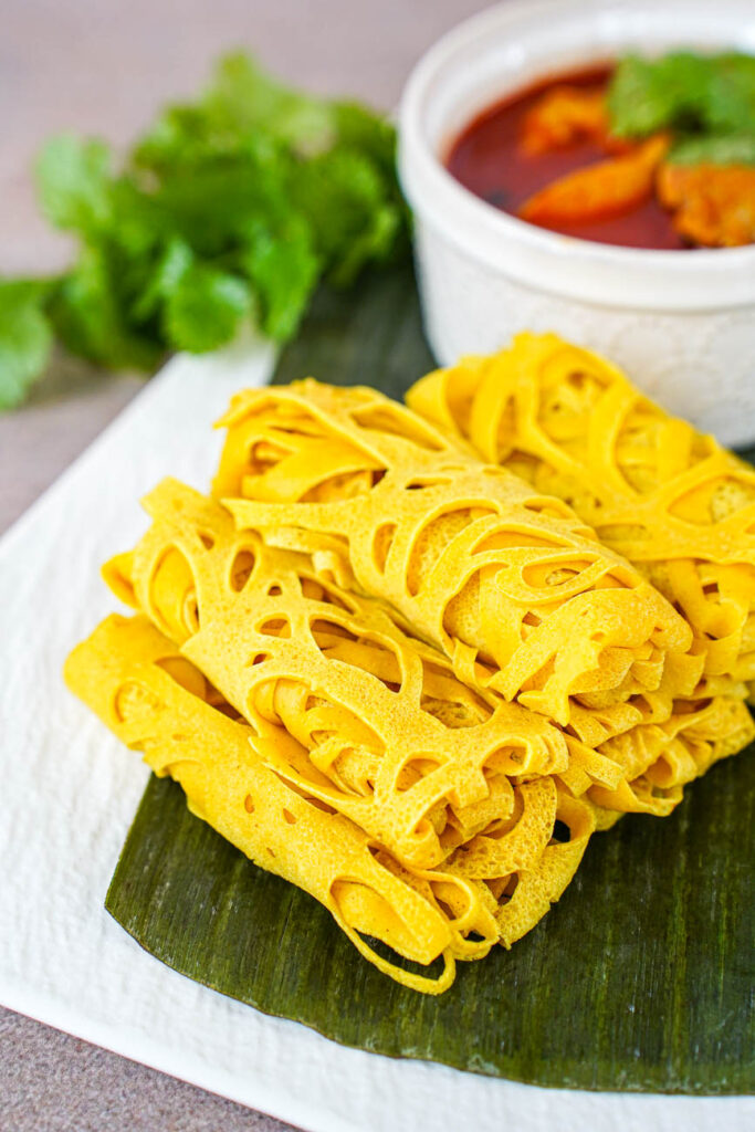 A rolled pile of Roti Jala on a plate with a banana leaf.