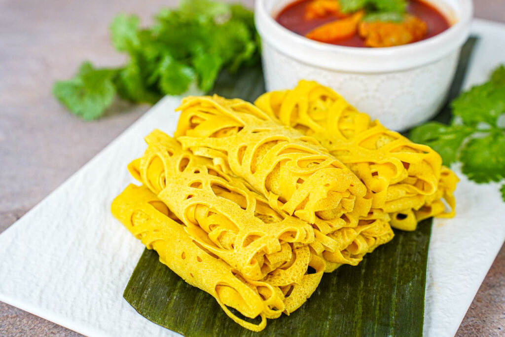A pile of rolled Roti Jala on a white plate with a banana leaf.