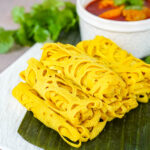 Six rolled Roti Jala next to a bowl of chicken curry.