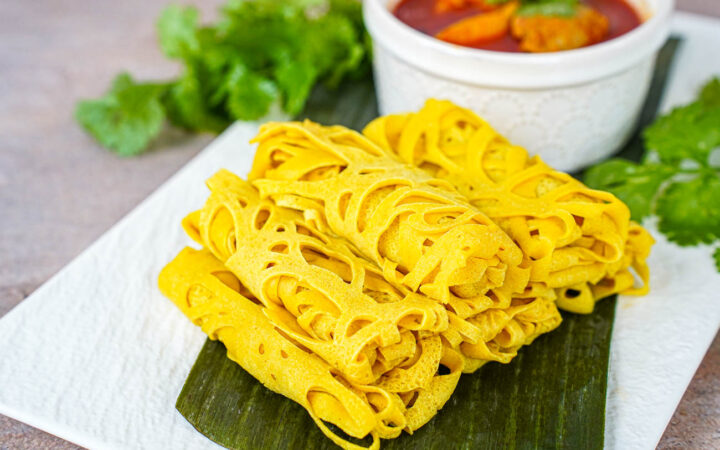 Six rolled Roti Jala next to a bowl of chicken curry.